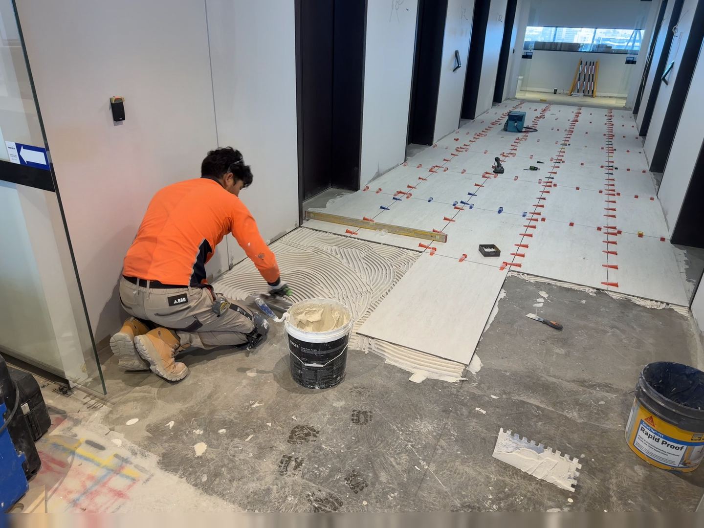 Tiler laying large-format floor tiles in a commercial corridor